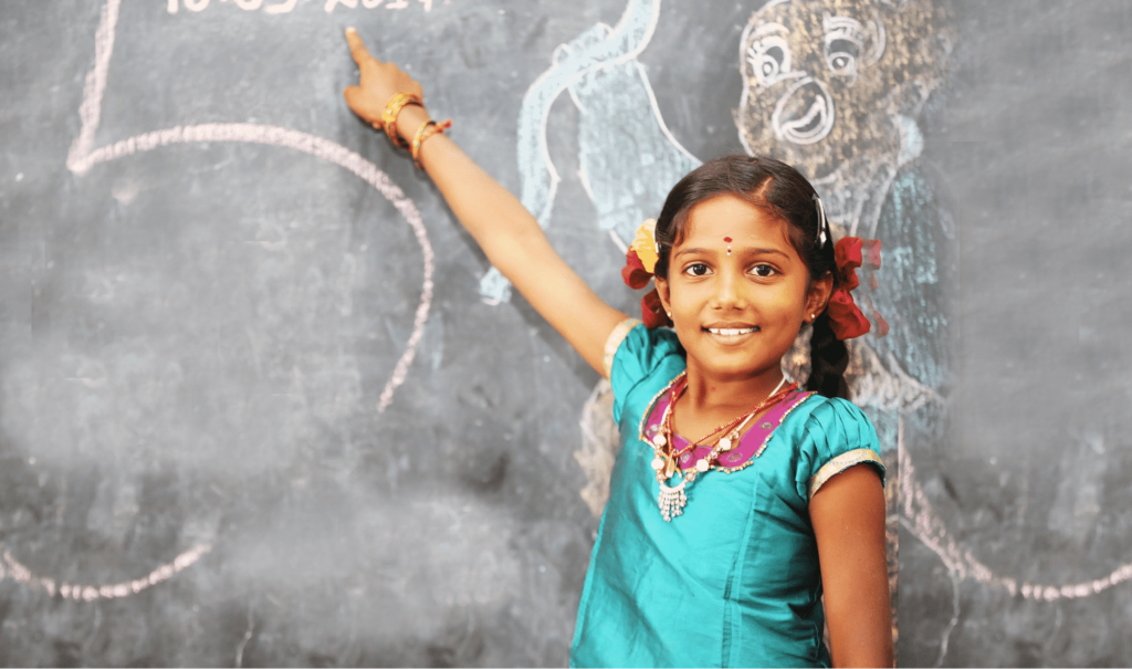 Girl smiling and pointing at artwork on chalk board
