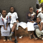 Students smiling outside with school work; the African SOUP supports teacher training in Uganda through digital literacy.