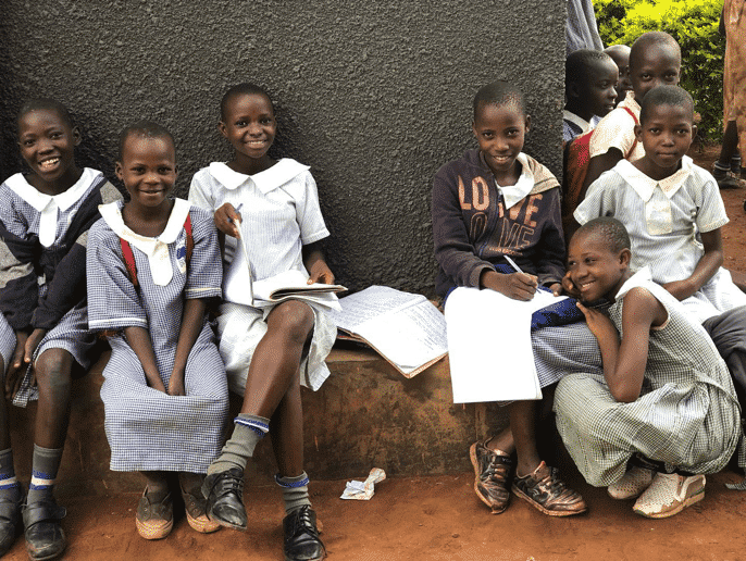 Students smiling outside with school work; the African SOUP supports teacher training in Uganda through digital literacy.