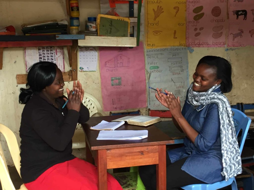 Two teachers laugh in their classroom. Dignitas is supporting a transition to online learning in Kenya.