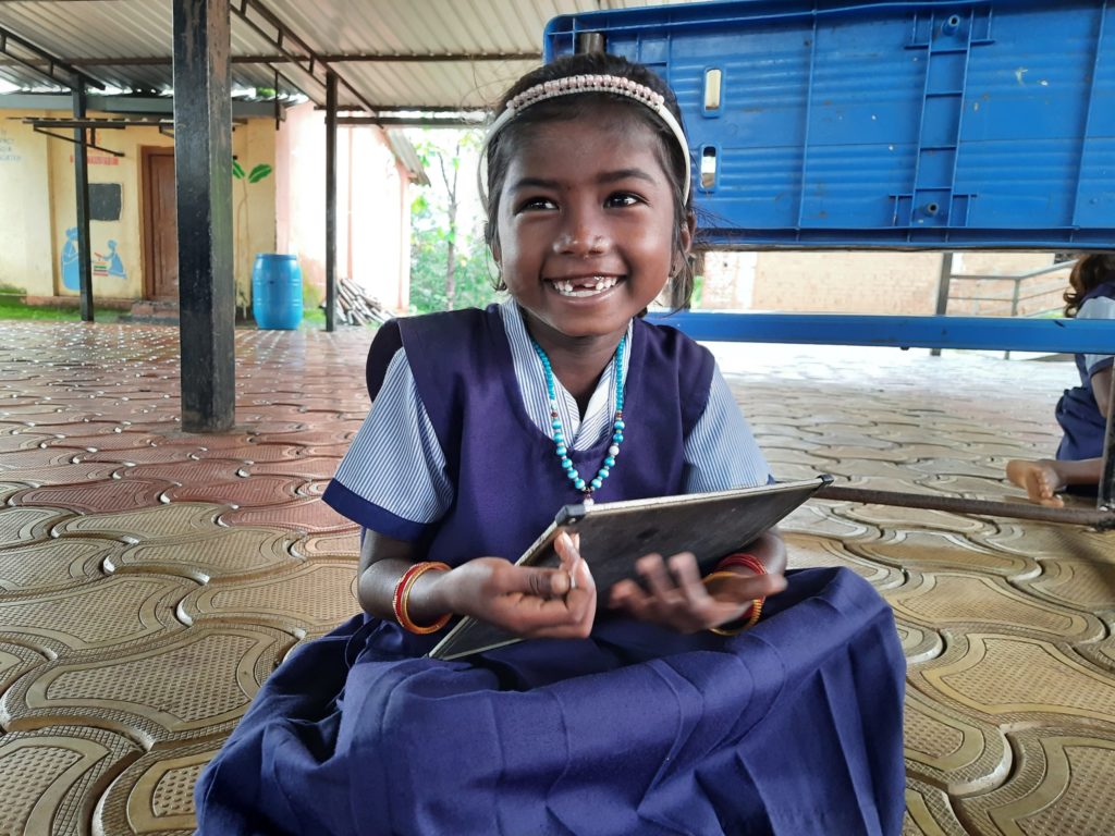 Child smiling with tablet; Learning Links Foundation supports girls in STEM in India.