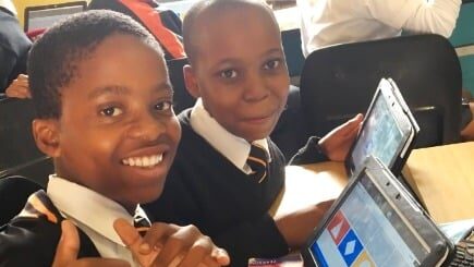 Two boy students giving the thumbs up and working on touchscreen tabelt