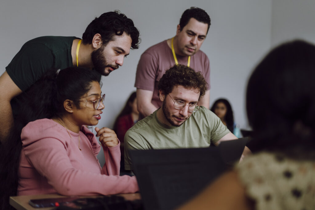 Team4Tech volunteers participating in skills-based volunteering project in Brazil. Four volunteers gather around a laptop to collaborate/